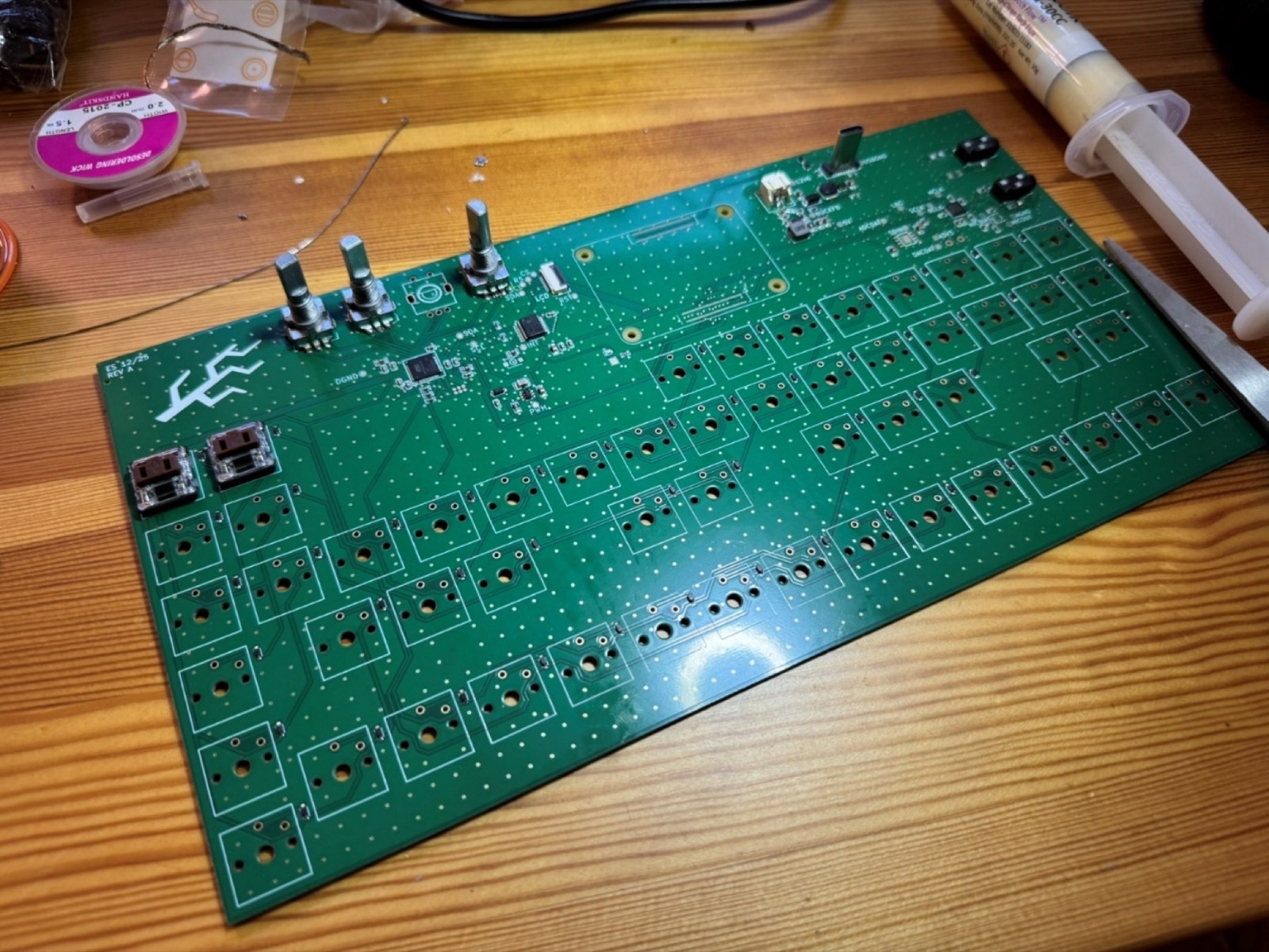 Large green validation circuit board on a wooden desk, with three rotary encoders fitted and most small components already placed