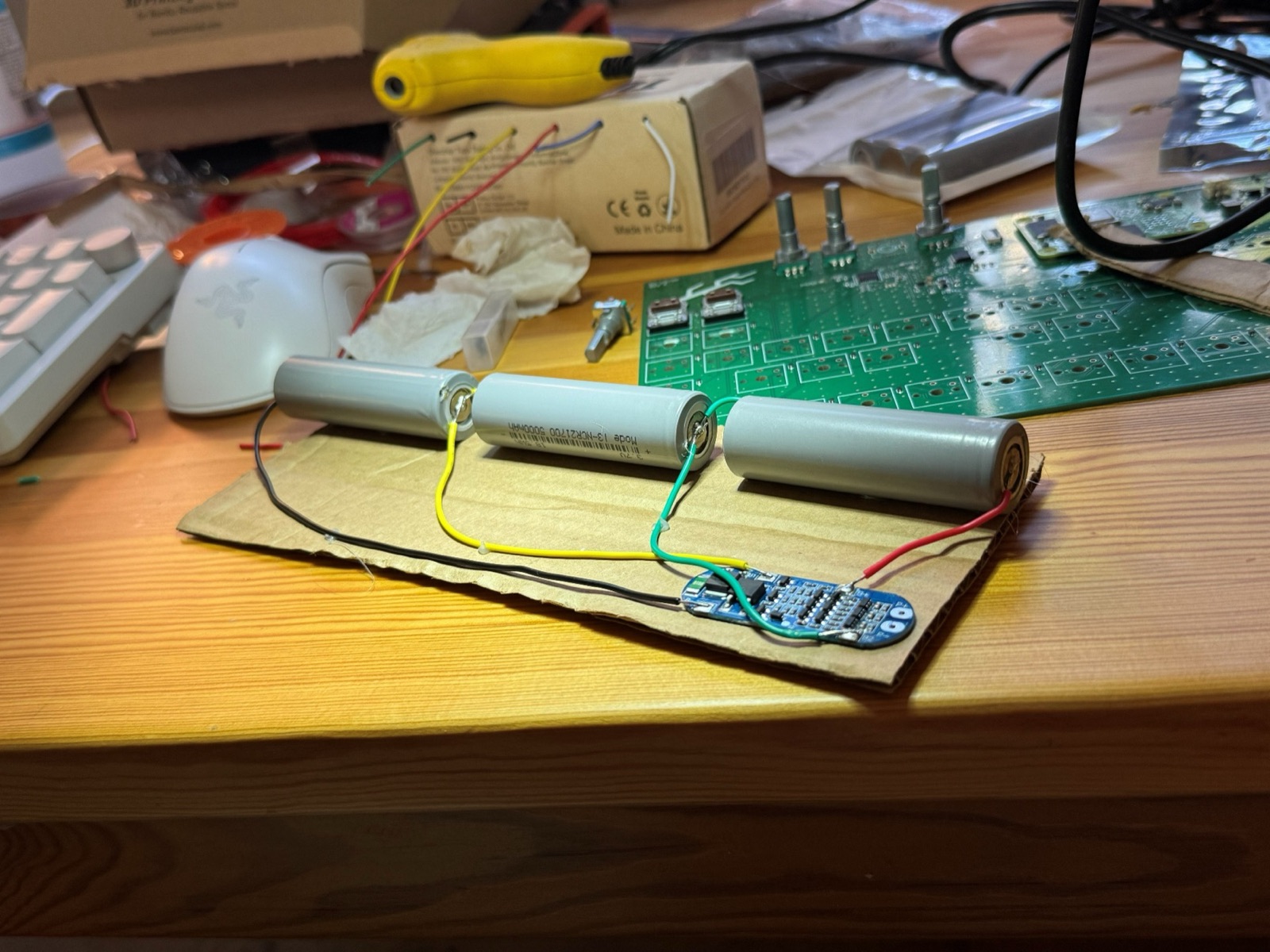 Three cylindrical lithium cells wired in series to a small battery management board on a piece of cardboard