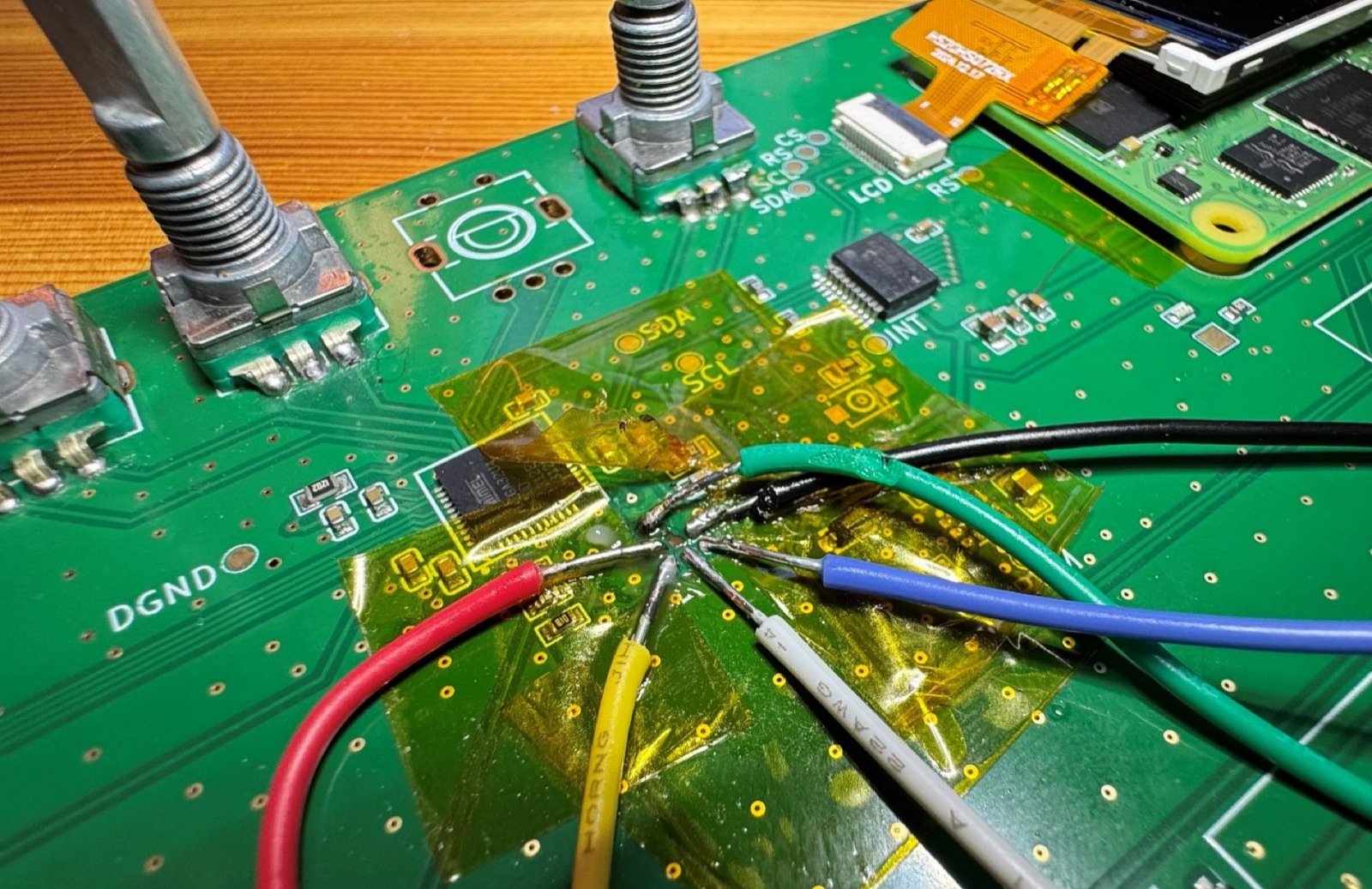 Close-up of coloured wires soldered to programming pads next to the keyboard controller chip, with a rotary encoder above