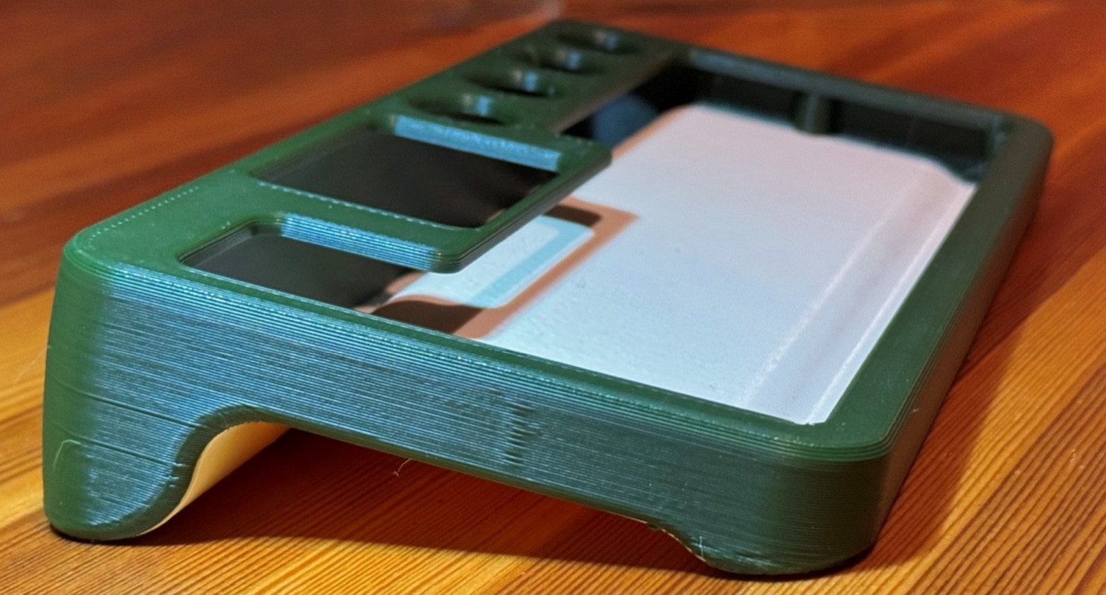 Dark green 3D-printed shell with a white inner tray, seen from the front edge with the display recess and knob holes visible