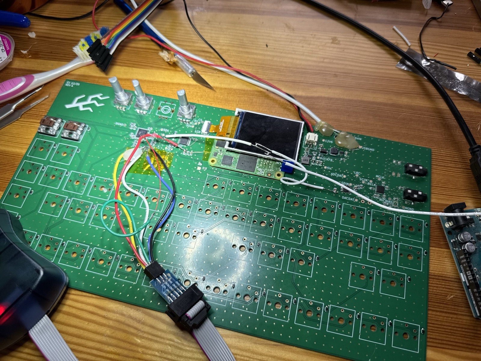 Validation board with a ribbon programmer cable and a bundle of coloured wires soldered to tiny pads near the keyboard controller chip