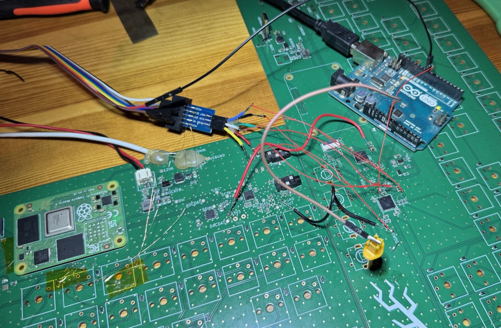 An Arduino injecting a clock signal into the keyboard chip via a thin wire, next to a Compute Module 4 lying on the board